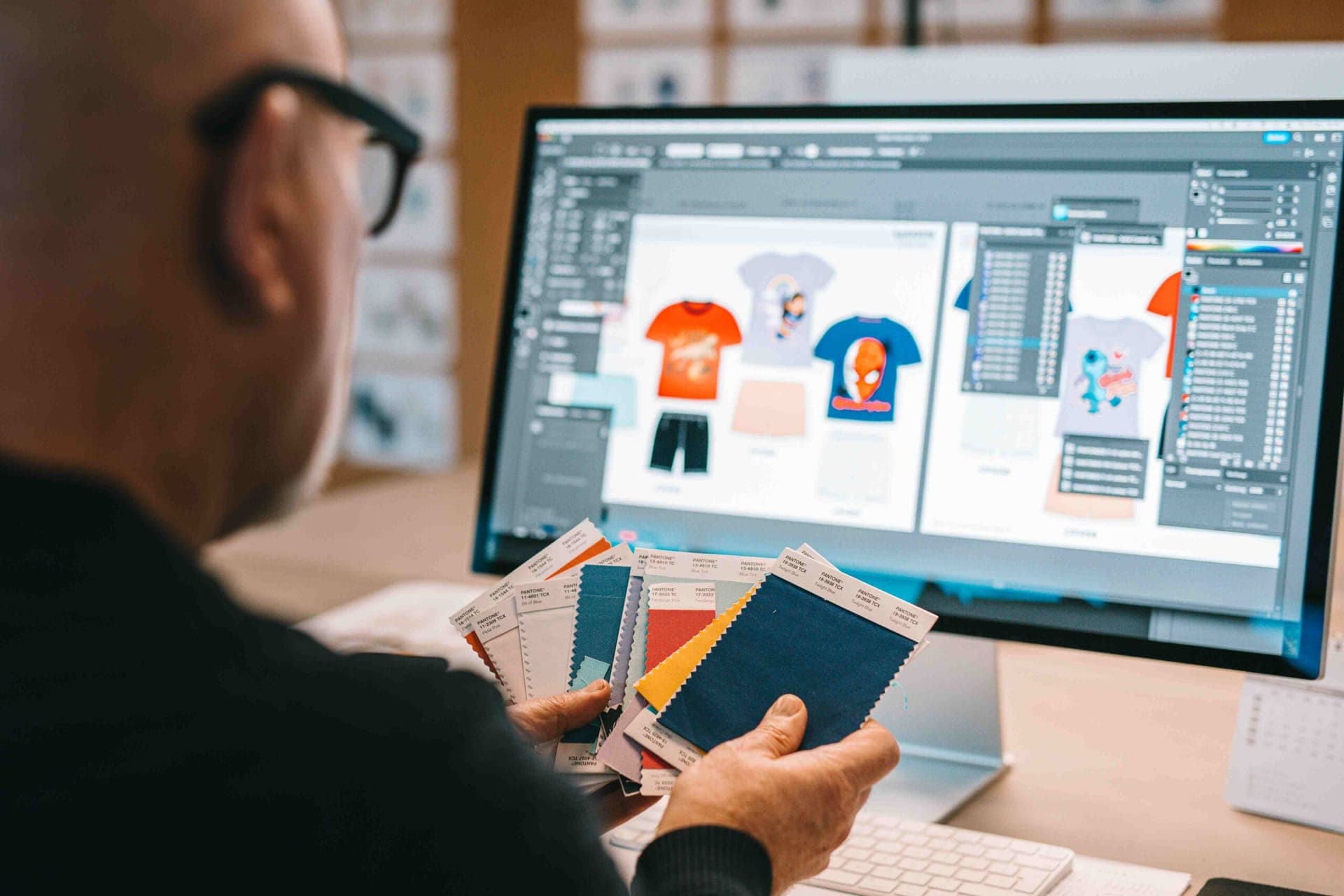 Designer holding Pantone fabric swatches in front of a screen with licensed kids' t-shirt designs
