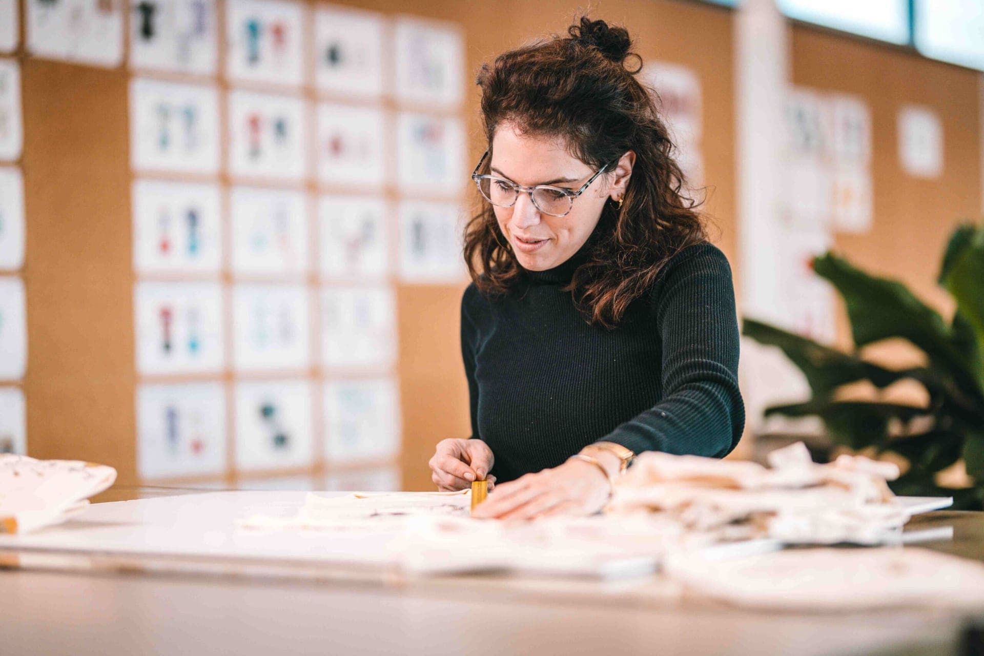 Designer working with fabric at a worktable in front of a wall of garment designs
