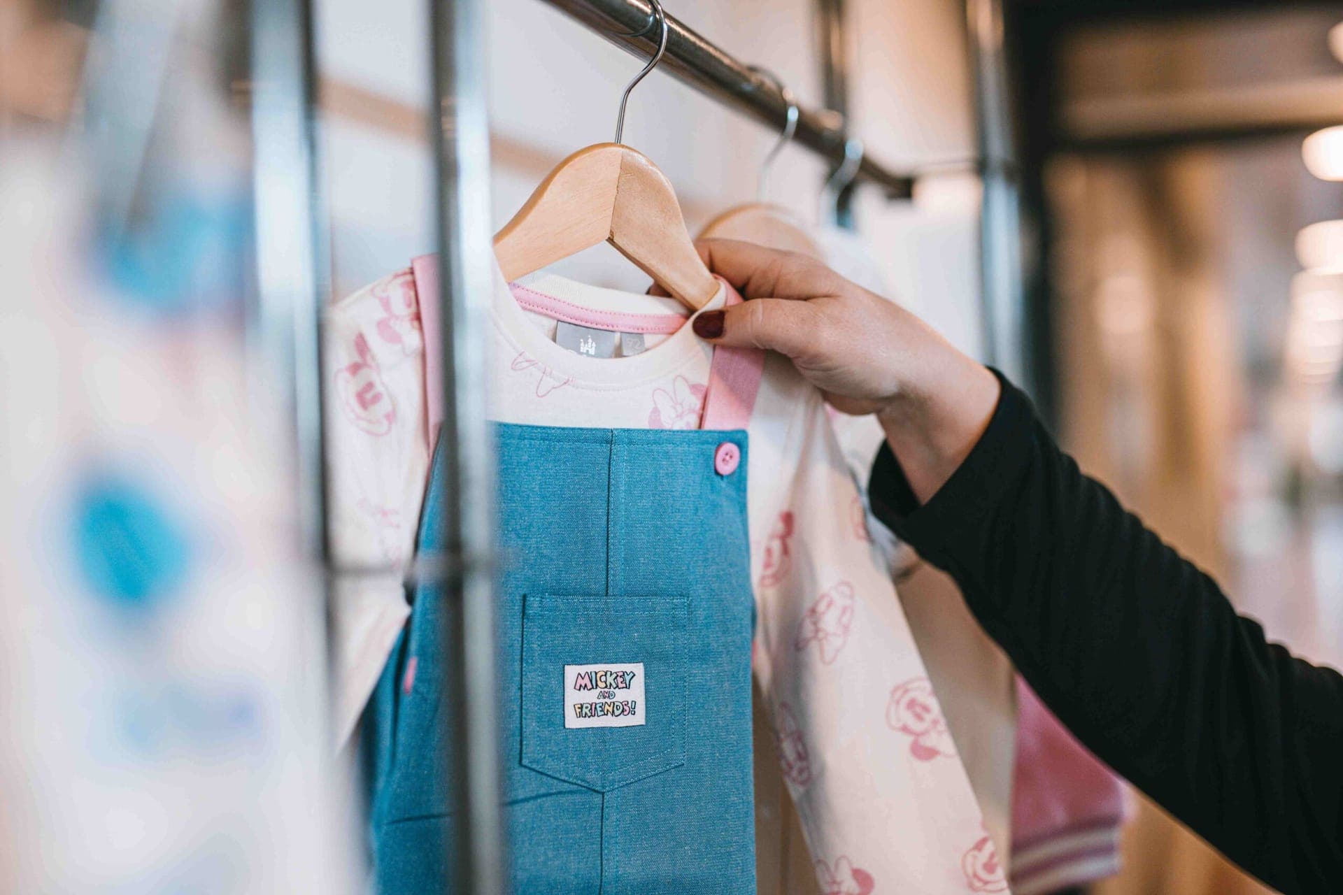 Close-up of a "Mickey and Friends" label on a denim dungaree dress, next to a top with a Minnie Mouse print